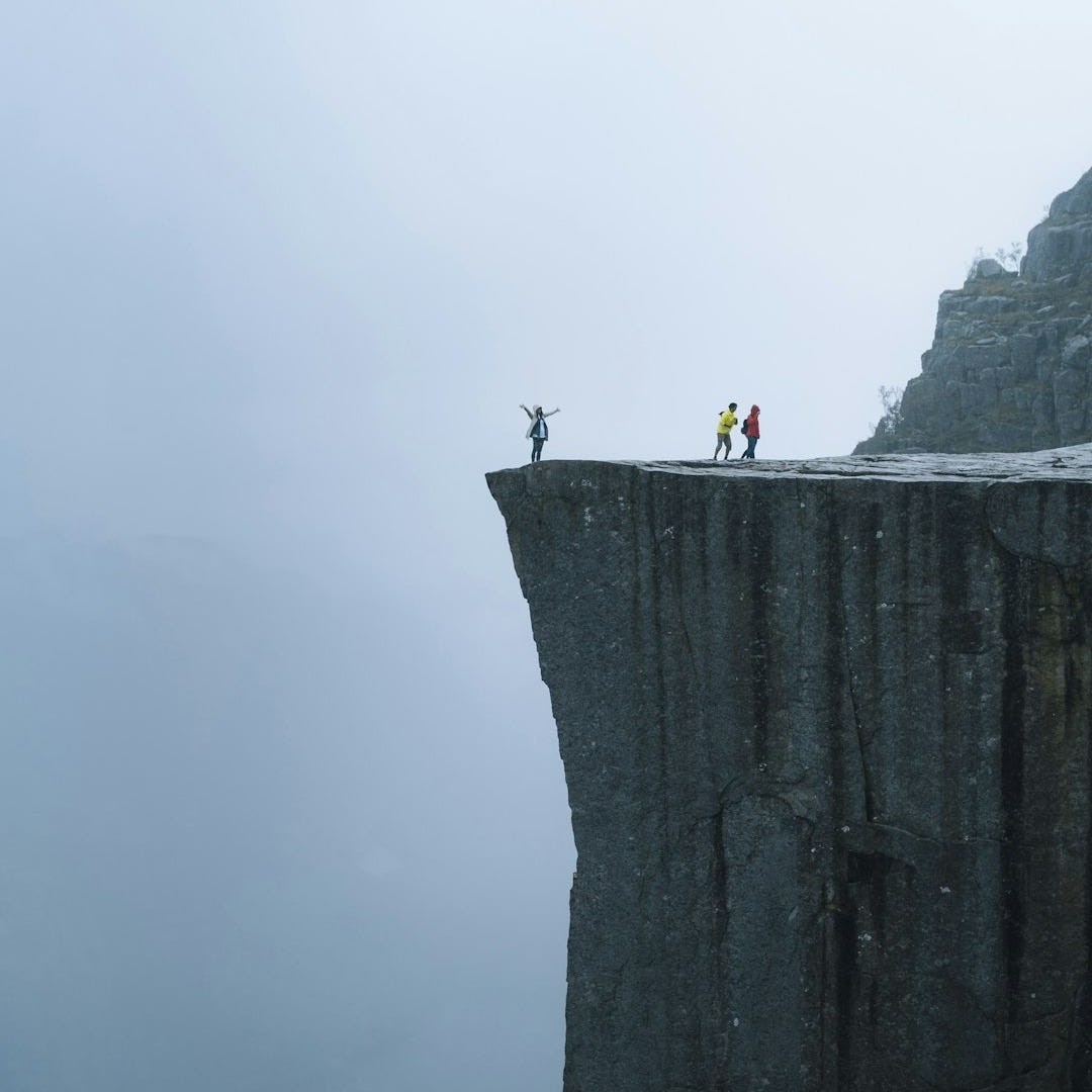 three persons standing near the edge of a cliff during day