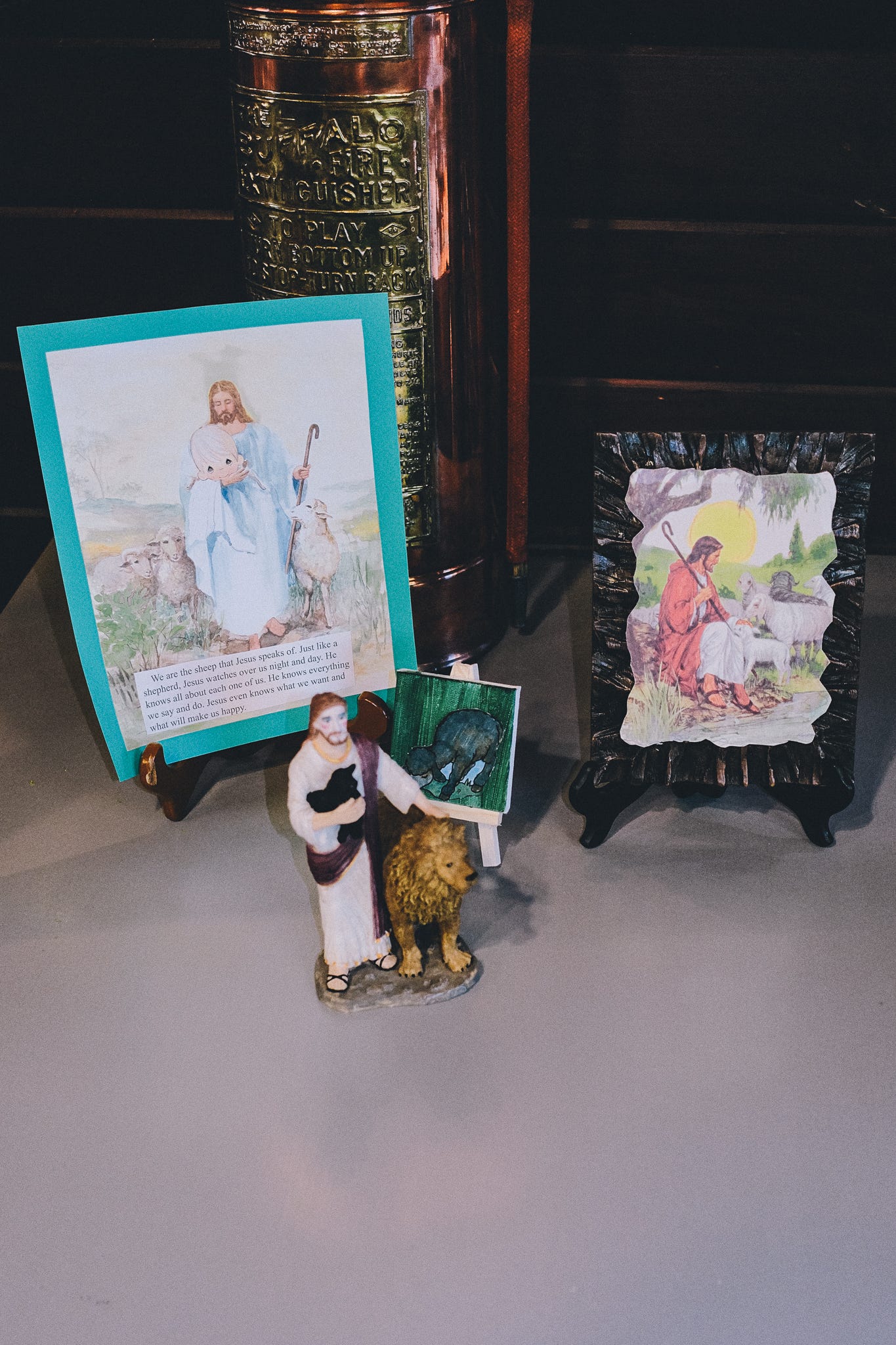 a table has several different pictires of JEsus holding sheep, with at least one of them being black