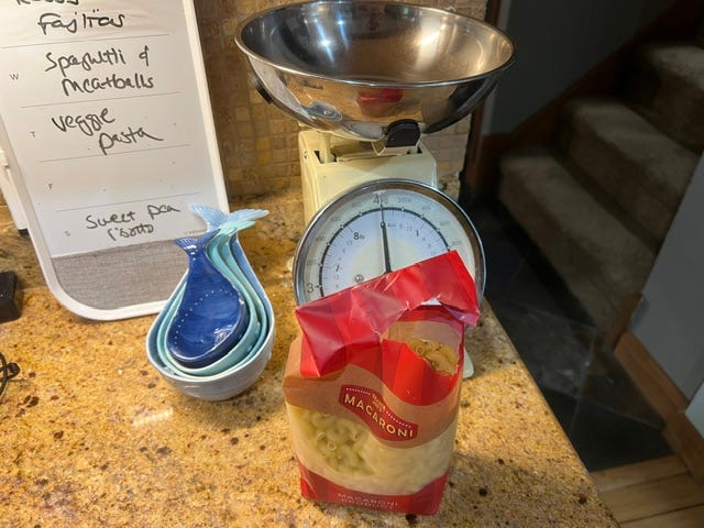 A bag of dry macaroni noodles in front of an old fashioned scale