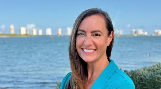 Emily Gregory smiles as she poses in front of the Intercoastal Waterway (I think?) across from a city skyline. 