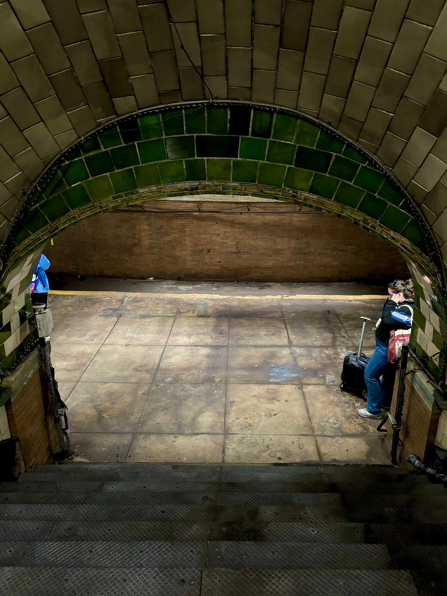 A green arch caps a white tile ceiling over a stairway down to the platform.