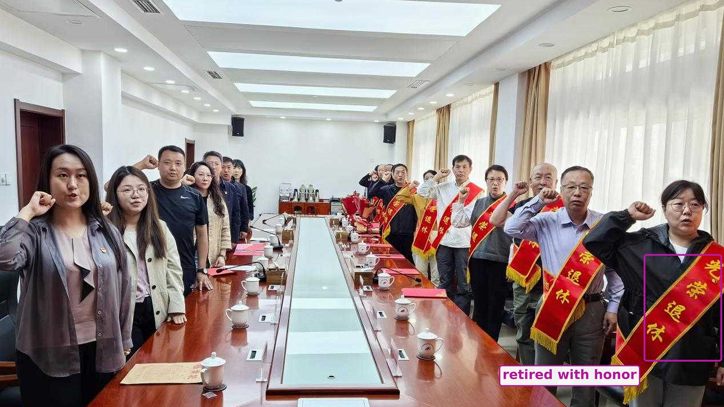Retirees in red sashes and their colleagues around a long conference table, right fists raised; the sashes read retired with honor.