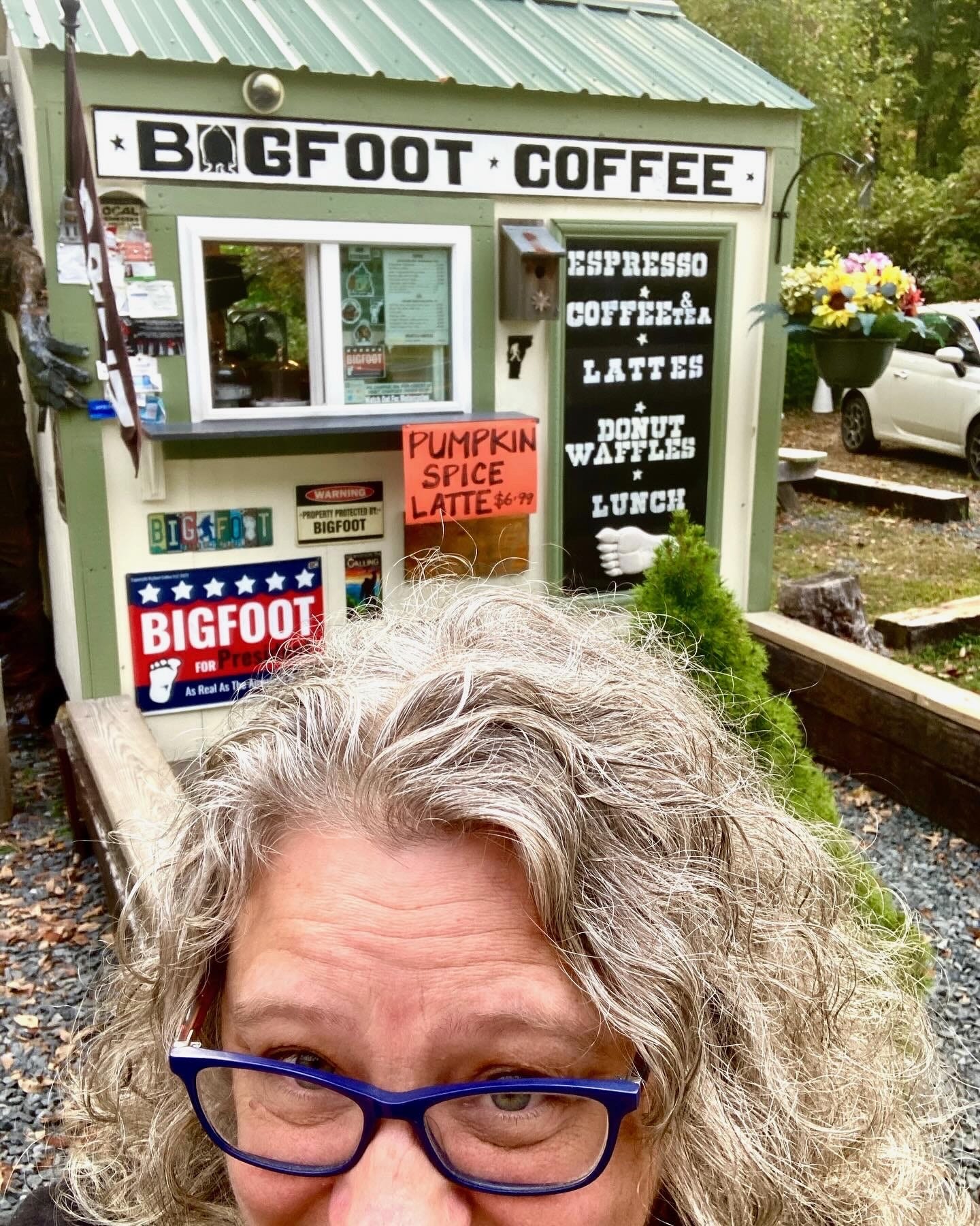 selfie of middle-aged white person in front of a tiny booth that says "bigfoot coffee" and advertises pumpking spice lattes and other drinks. selfie of middle-aged white person in front of a tiny booth that says "bigfoot coffee" and advertises pumpking spice lattes and other drinks.