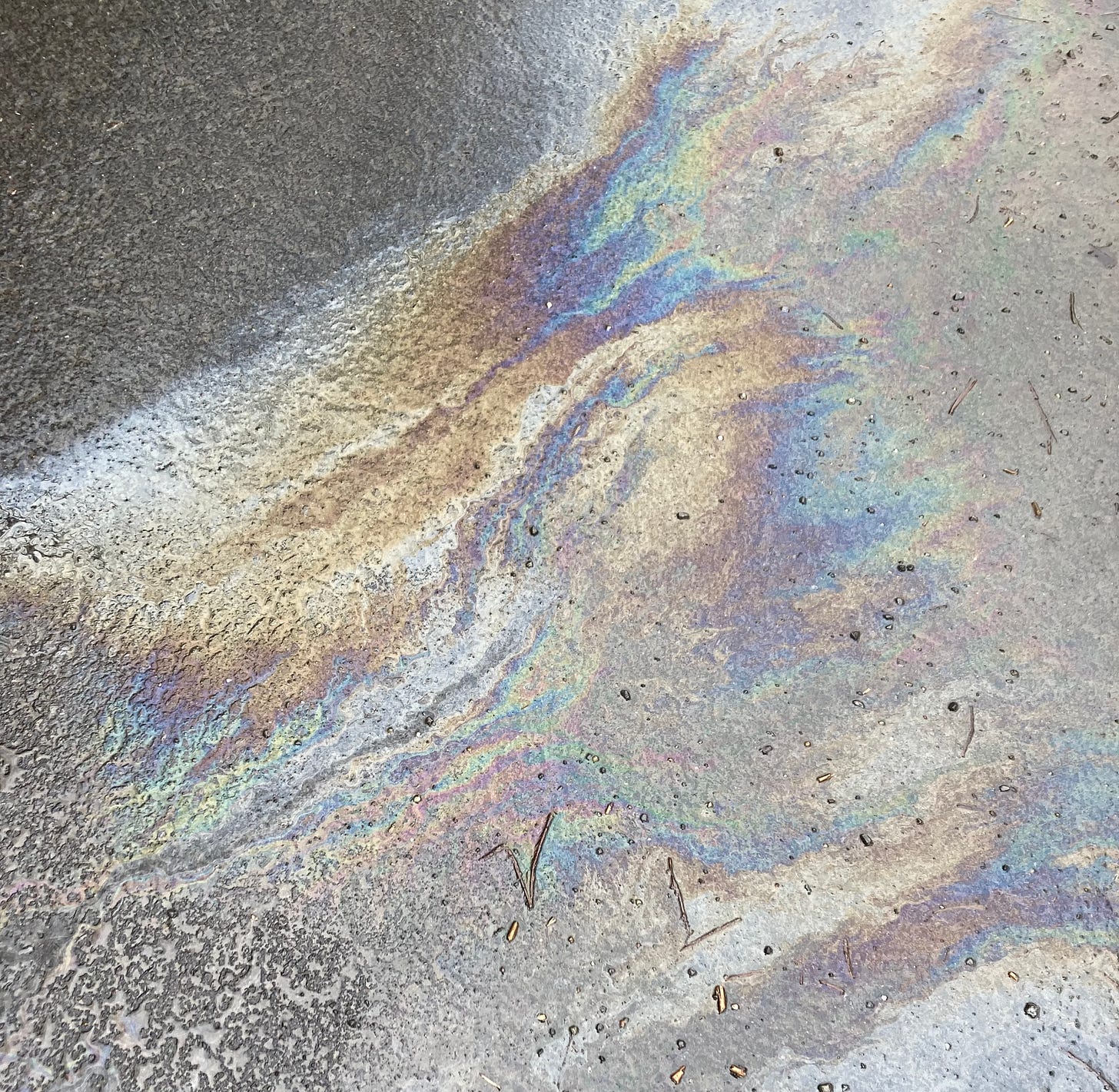 shimmering iridescent rainbow from oil mixing with water on asphalt
