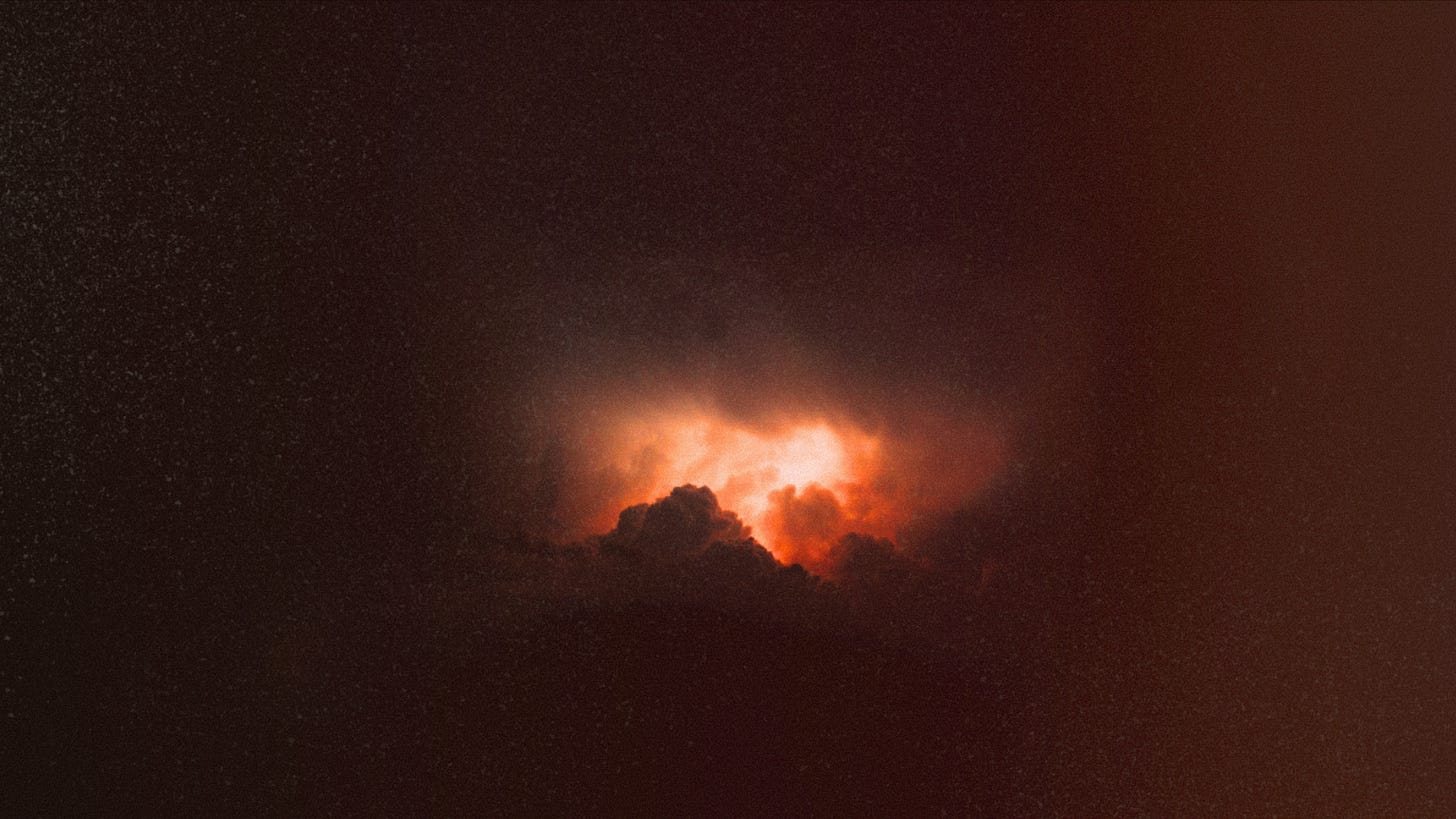 a very dark sky with a single thunderhead backlit by reddish orange light