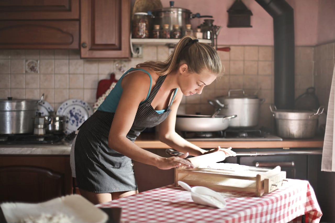 A young woman rolls dough on a bread board in the kitchen. A young woman rolls dough on a bread board in the kitchen.