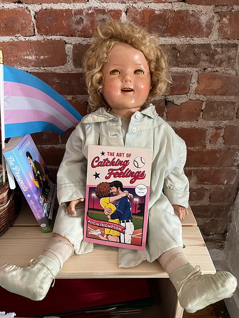 Three images of a haunted doll named Luci, one holding up LOVE IN THE TIME OF SERIAL KILLERS and a knife, one holding up WITH LOVE, FROM COLD WORLD, and one holding up THE ART OF CATCHING FEELINGS