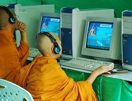 This may contain: two monks sitting in front of laptops with headsets on and one is listening to music