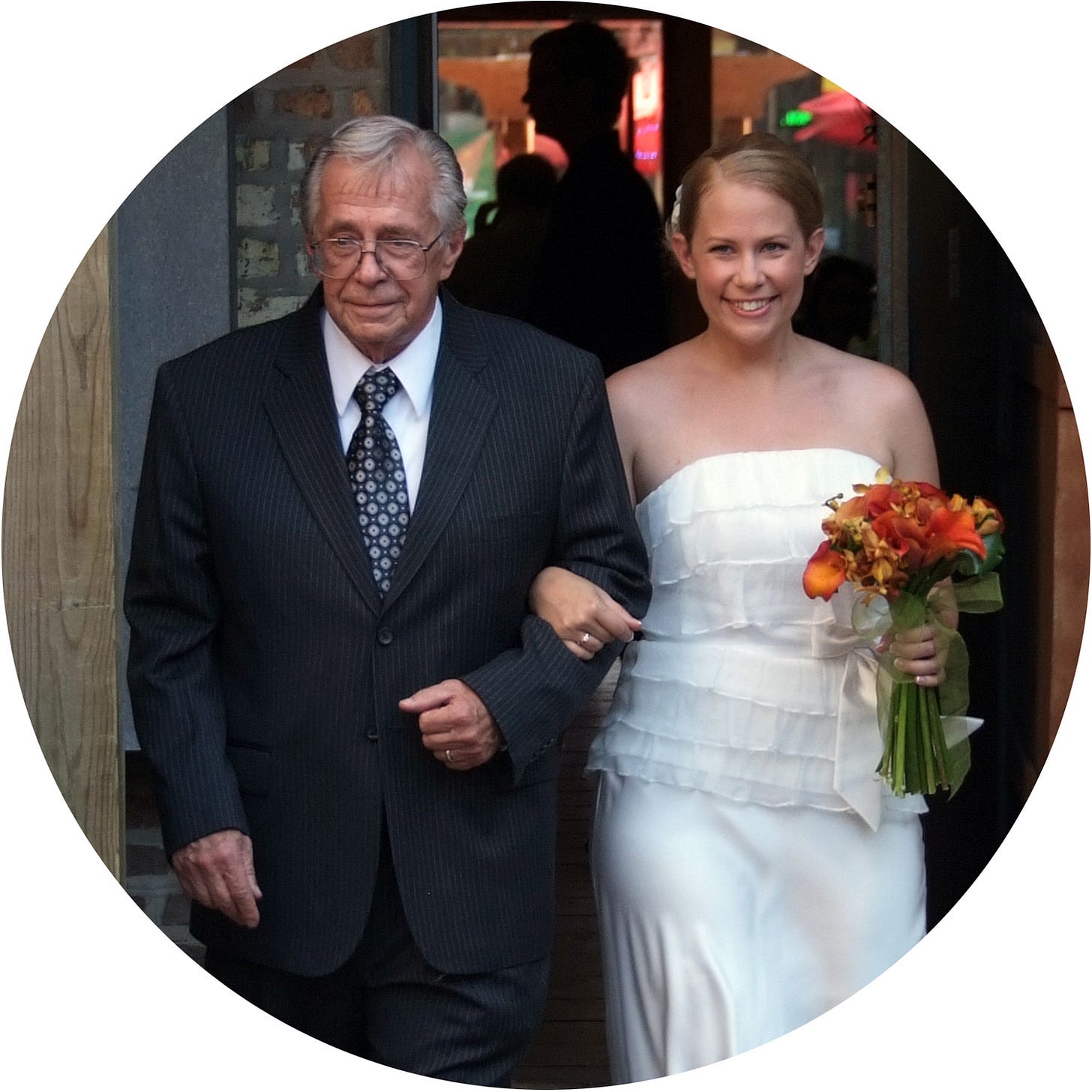 Bride in a white dress walking arm in arm with an older man in a dark suit.