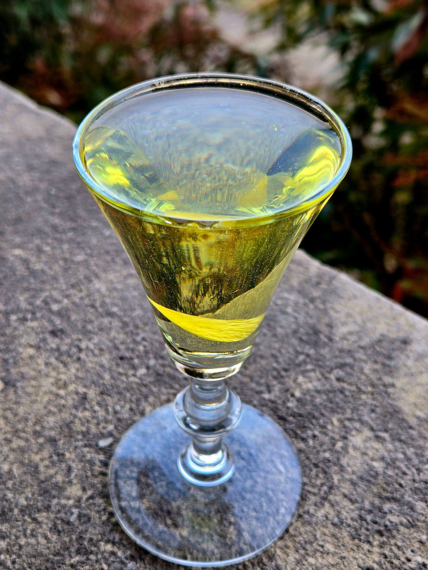 Alaska cocktail with leman disc garnish in a sherry glass atop a stone wall.