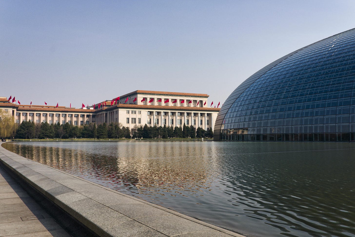 The Great Hall of the People in Beijing, red flags along its roofline, mirrored in a reflecting pool.