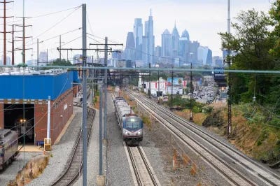 Amtrak train on tracks with Philadelphia, Pennsylvania skyline in background.