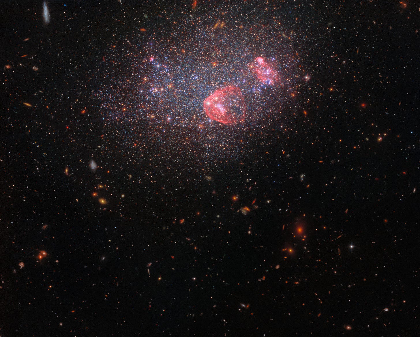 A field of galaxies. UGC 8091 is at the top and center of the image. It appears as a haze of stars through which more distant galaxies are visible. Two A field of galaxies. UGC 8091 is at the top and center of the image. It appears as a haze of stars through which more distant galaxies are visible. Two