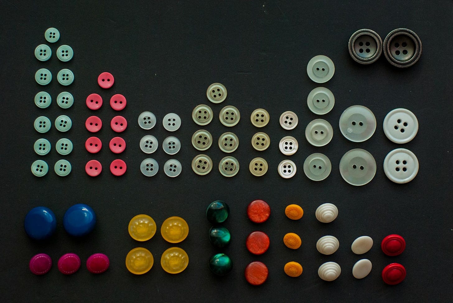 A variety of button shapes, colors, and sizes appears on a dark gray background. A variety of button shapes, colors, and sizes appears on a dark gray background.
