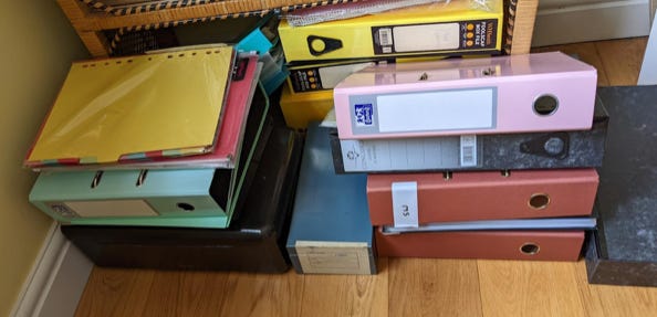 A pile of lever arch files sit on the floor.