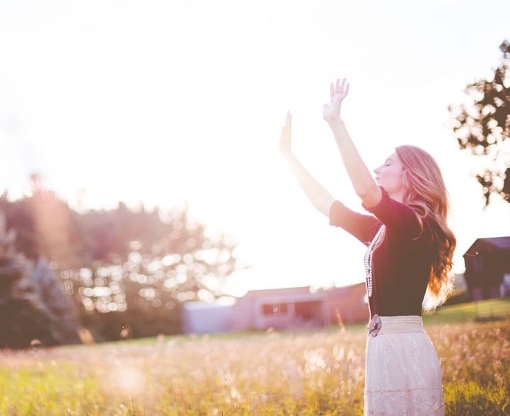 woman hands up in front of green meadows