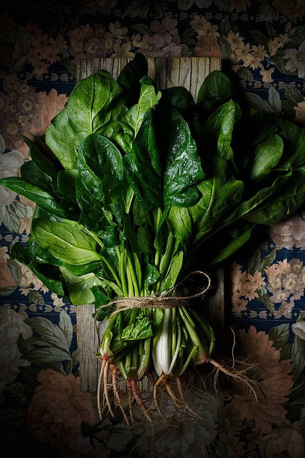 This may contain: a bunch of green leafy vegetables sitting on top of a wooden table next to a wall