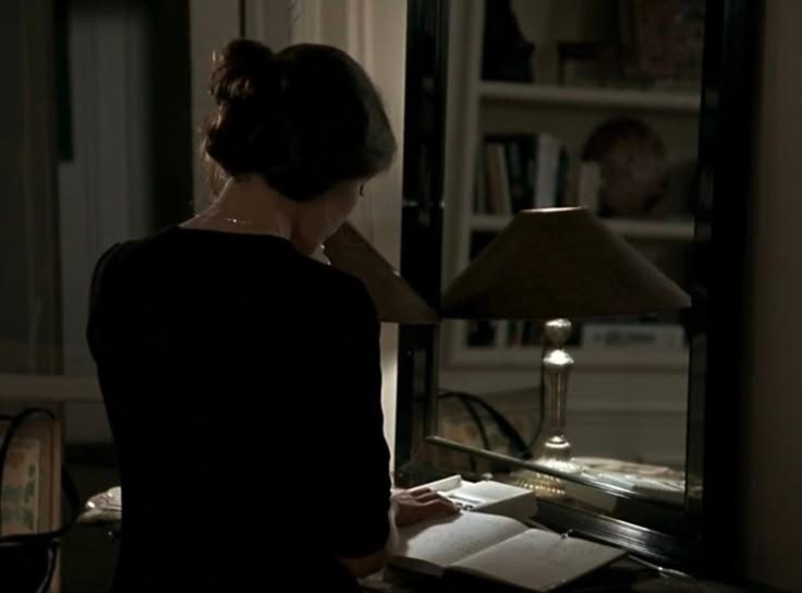 This may contain: a woman sitting at a desk in front of a mirror with a lamp on it