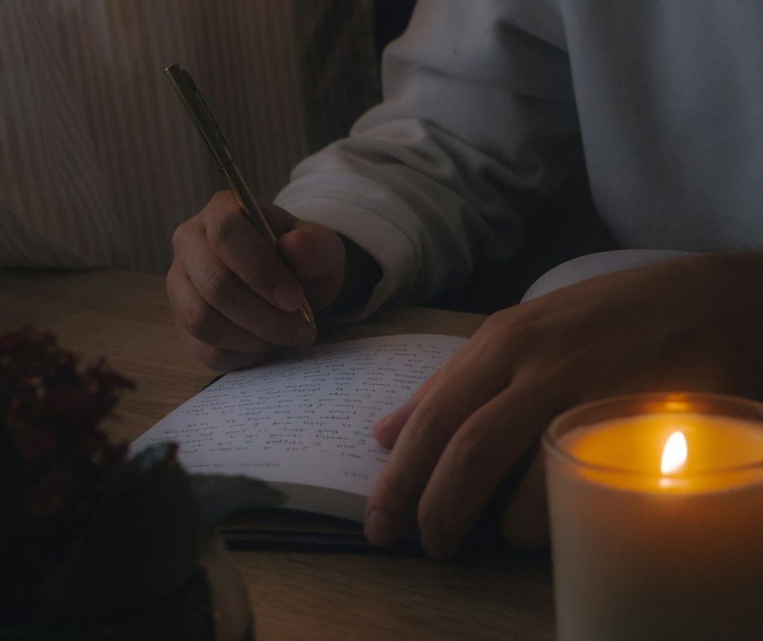 a person sitting at a table writing in a notebook next to a lit candle a person sitting at a table writing in a notebook next to a lit candle