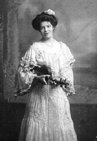 Woman in Edwardian dress carrying string instrument