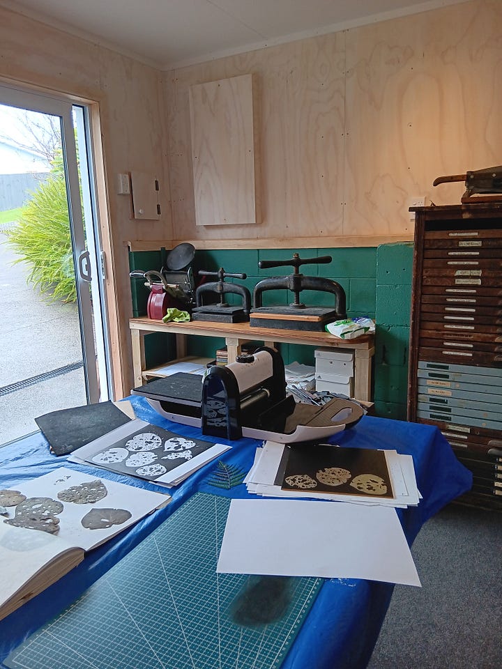 First photo: printing in progress with kawakawa leaves, book presses and an adana press in the background. Second photo an array of prints of text, ferns and kawakawa on handmade paper laid out to dry.