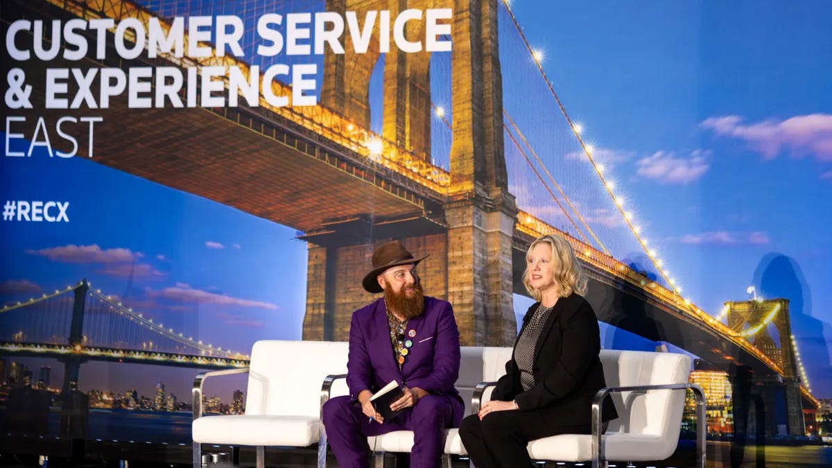 Two people sit on a stage for a fireside chat at a conference. Two people sit on a stage for a fireside chat at a conference.