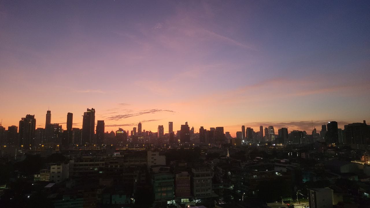 A purple, orange and pink sky at sunrise over a city where buildings are on the horizon.