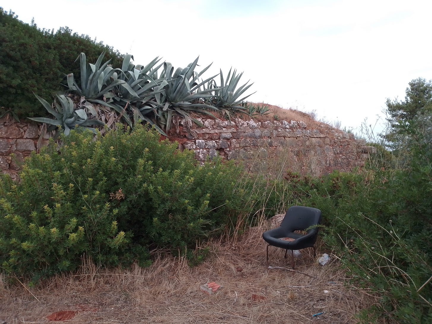 A discarded black chair sits in front of the ruined wall of an old fort.