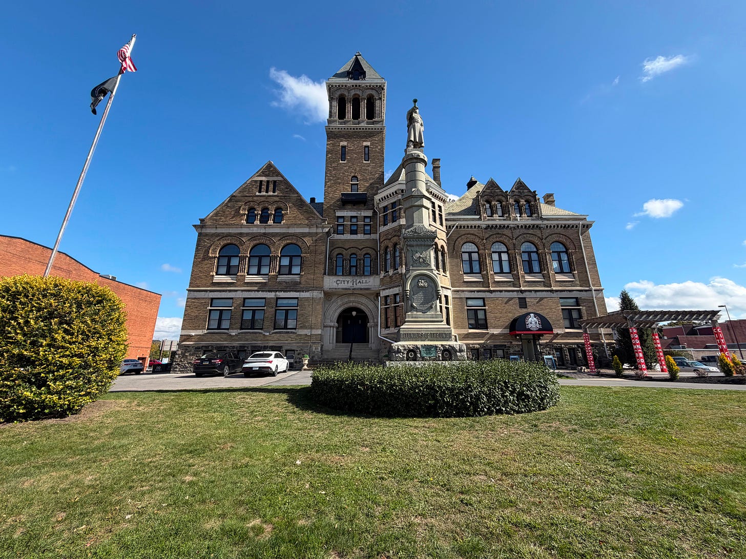 A large brick building with a flagpole and some shrubbery in front