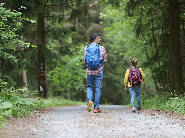 Father and daughter walking side-by-side on a nature trail Father and daughter walking side-by-side on a nature trail