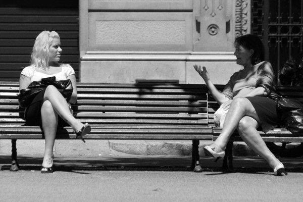 This may contain: two women sitting on a bench talking to each other