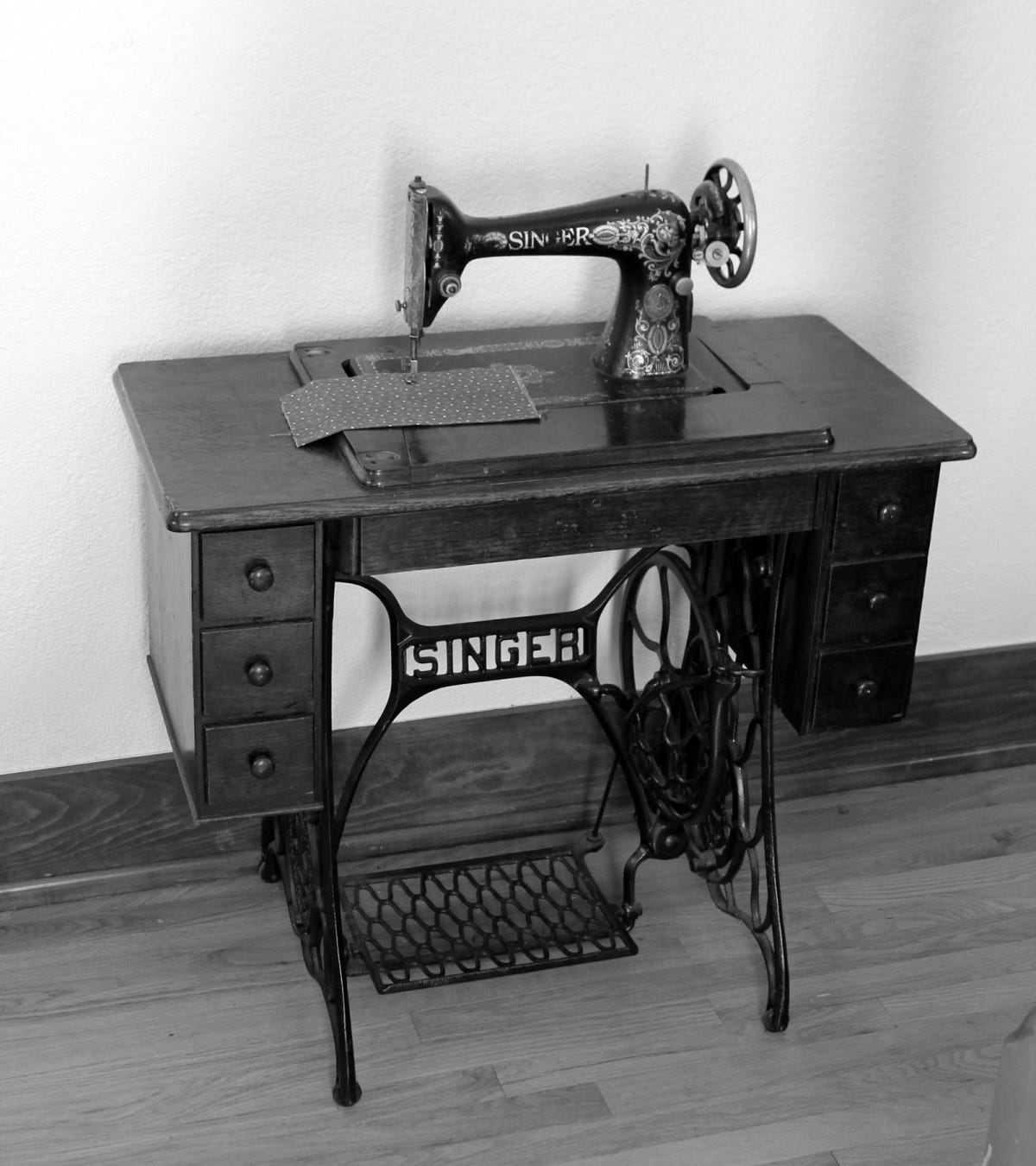 A black and white photo of a wrought iron Singer brand table sewing machine.