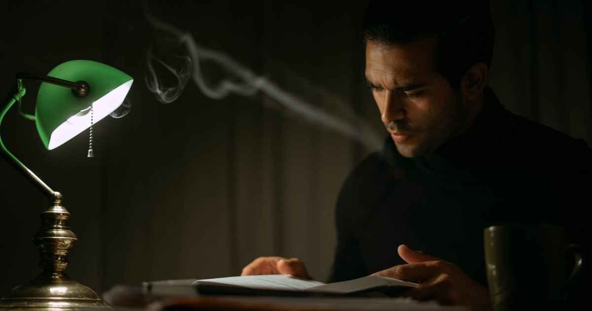 Pensive man reading by lamp light in an office at night Pensive man reading by lamp light in an office at night