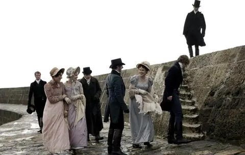 Group of Regency men and women walking along a stone wall at the seaside. 