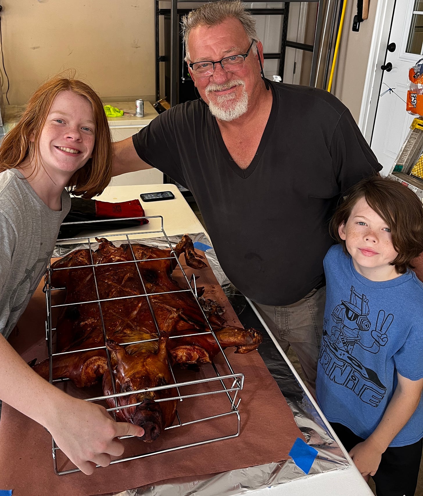 A grandfather and two grandsons with a roasted pig in a cage grill