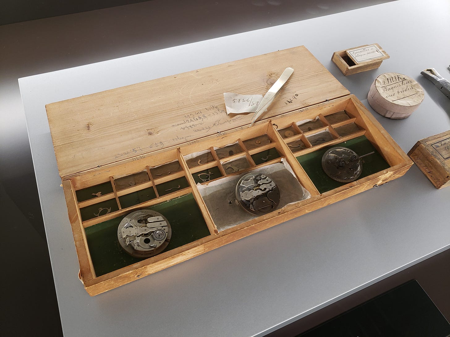 Wooden watchmaker’s bench with compartments holding vintage tools, watch parts, and handwritten notes.
