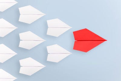 A formation of paper planes with a red leader, to show a brand influences and leads others in a blog by Joanne Tan, business branding expert,10PlusBrand.com