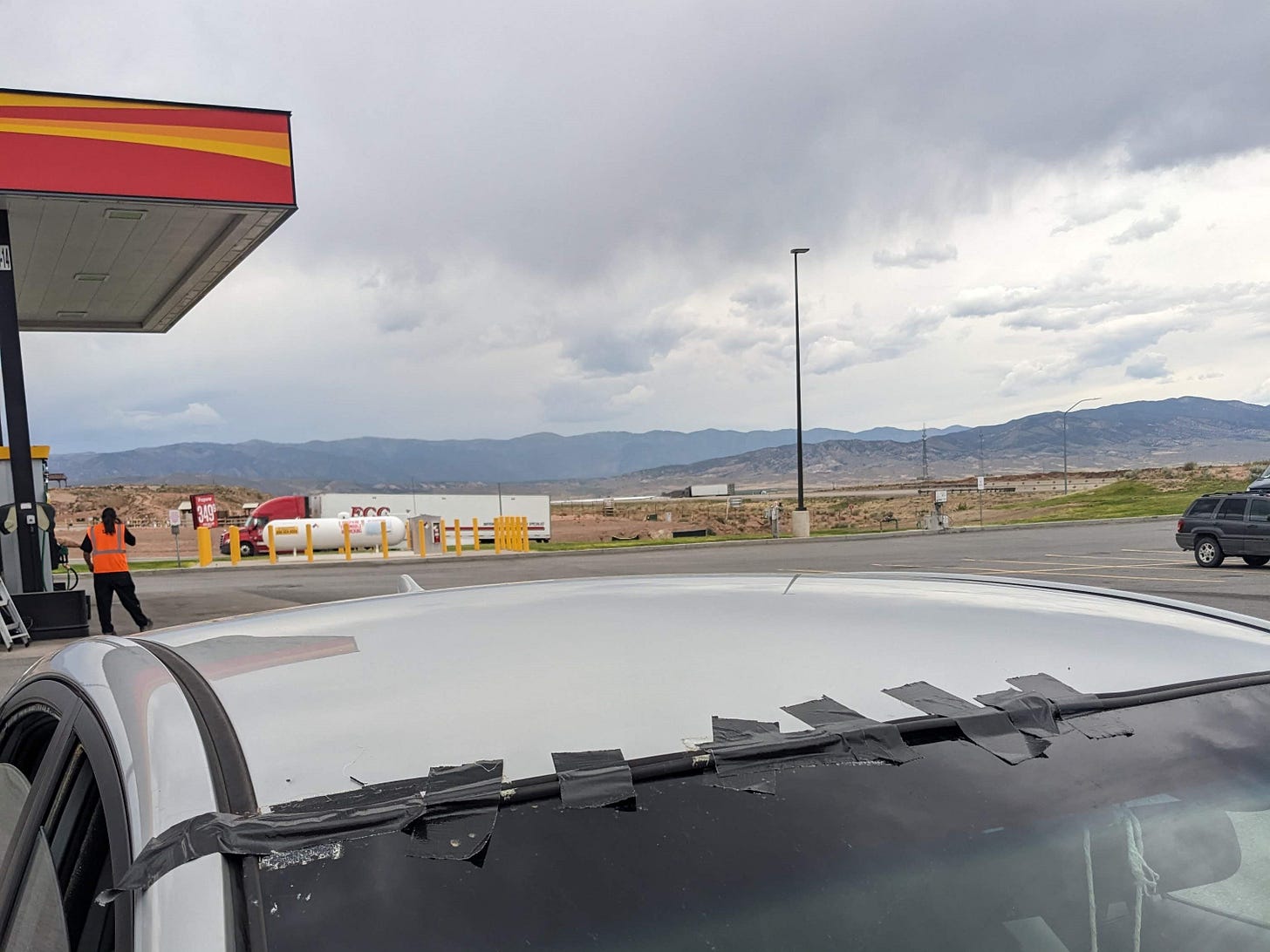 car parked at a gas station. the top of the windshild is covered in about a dozen pieces of black duct tape.