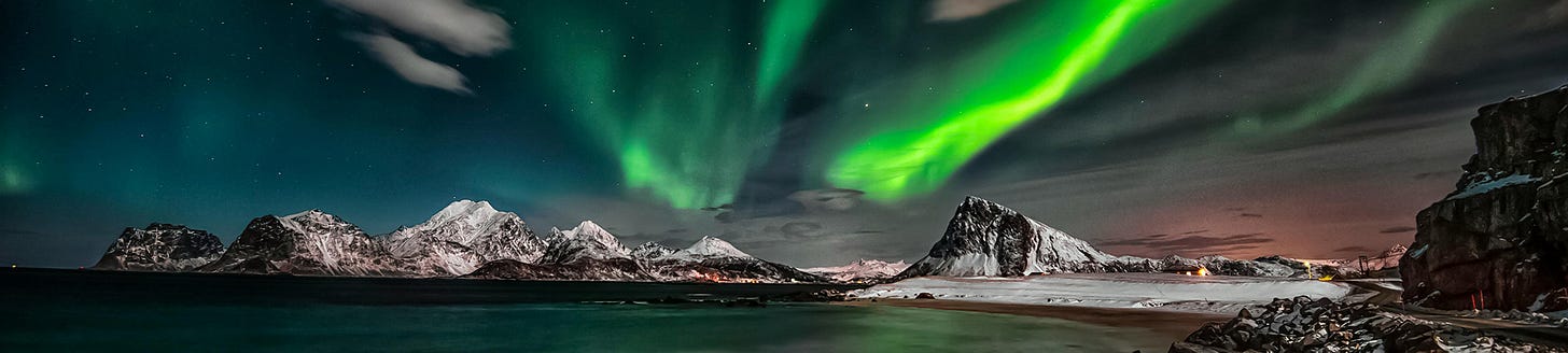 Green ribbons of aurora in the dark sky over snow covered mountains, which surround a bay Green ribbons of aurora in the dark sky over snow covered mountains, which surround a bay