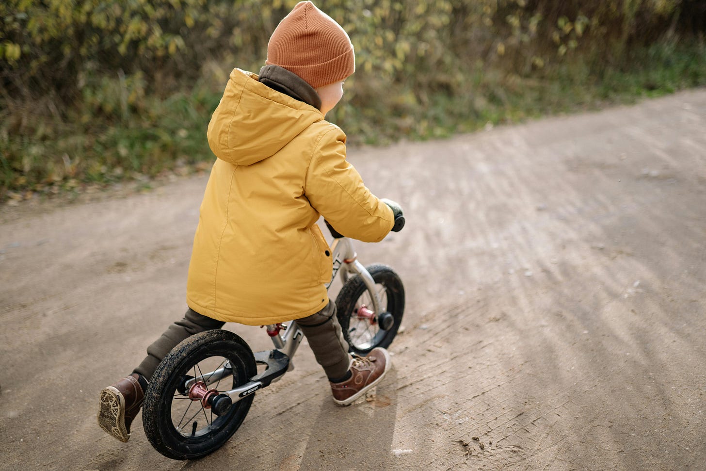 Free A child wearing a yellow jacket and beanie rides a bike on a dirt path outdoors. Stock Photo