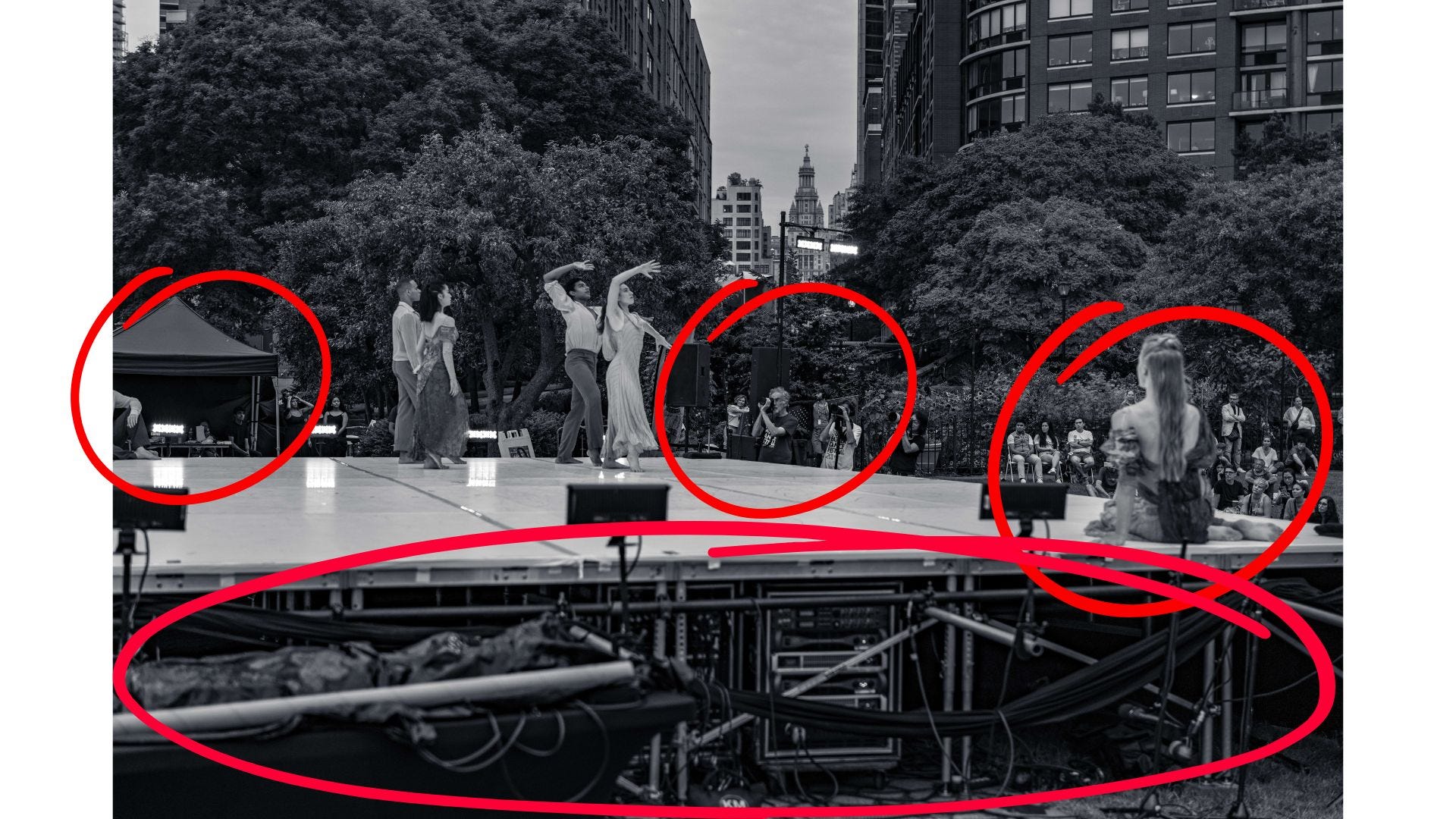Several dancers perform on stage in Battery Park with the audience watching from behind, framed by trees and New York City buildings in the distance. Several dancers perform on stage in Battery Park with the audience watching from behind, framed by trees and New York City buildings in the distance.