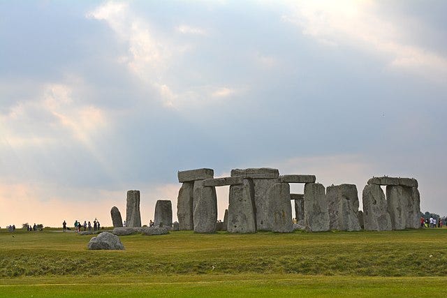 Image shows the standing stones of Stonehenge in front of bright sky with clouds, seemingly at dusk.