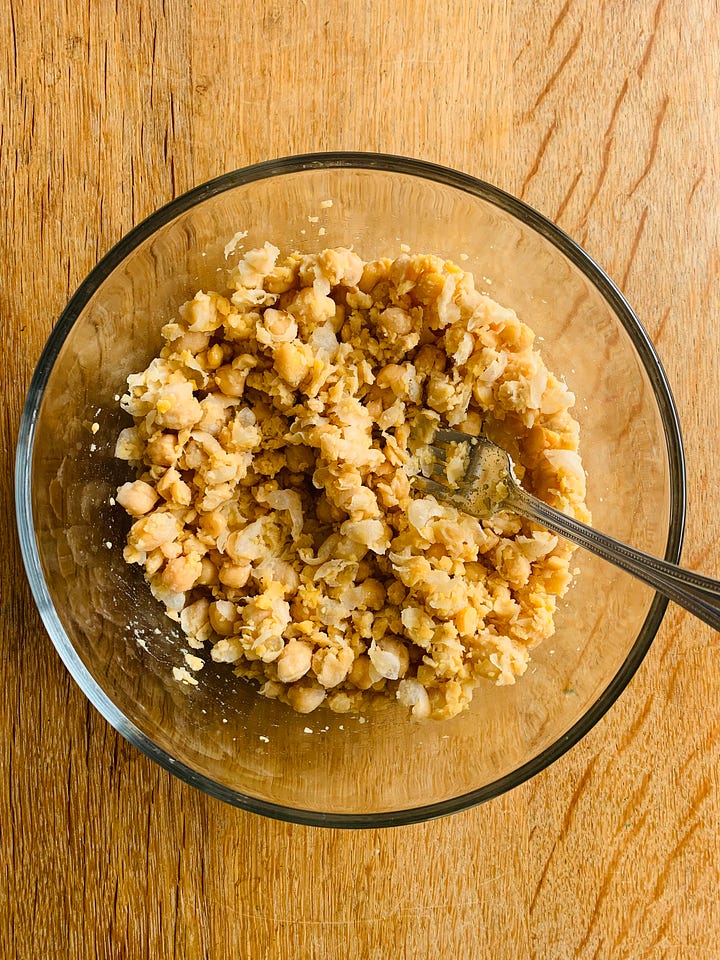 Mashed chickpeas in a bowl with salad ingredients.