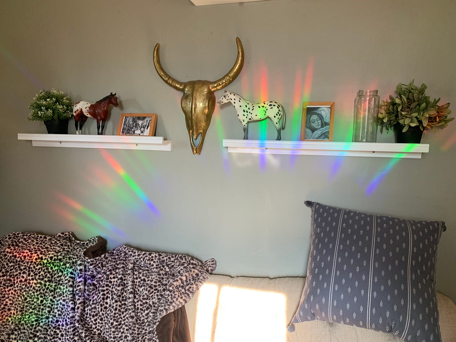 Above a couch and living room adornments on a shelf bursts a crescent of rainbow light.