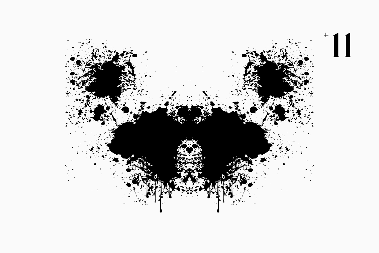 A bilateral, Rorschach-style inkblot specimen for the “In Other Words” series from The Subtext Review. The charcoal-black symmetrical splatter is centered on a cream paper background, labeled as Puzzle No. 11 in a classic serif typeface.
