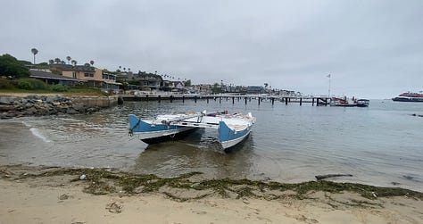 small voyaging canoe up on the sandy beaches on a gray chilly day. Our friend Kalani stuffing and trying to manage many bags and tools stuffed into a car seat. An uncle towing our boat with a side tie and a small engine boat used for paddling races.