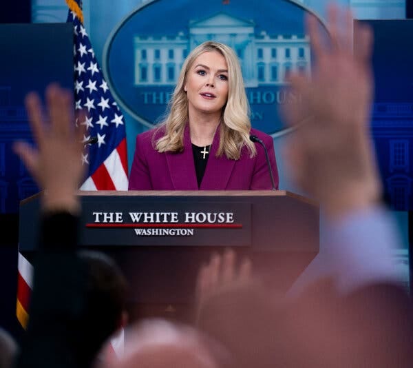 a blond woman behind a lectern with a purple jacket wearing a gold cross around her neck a blond woman behind a lectern with a purple jacket wearing a gold cross around her neck