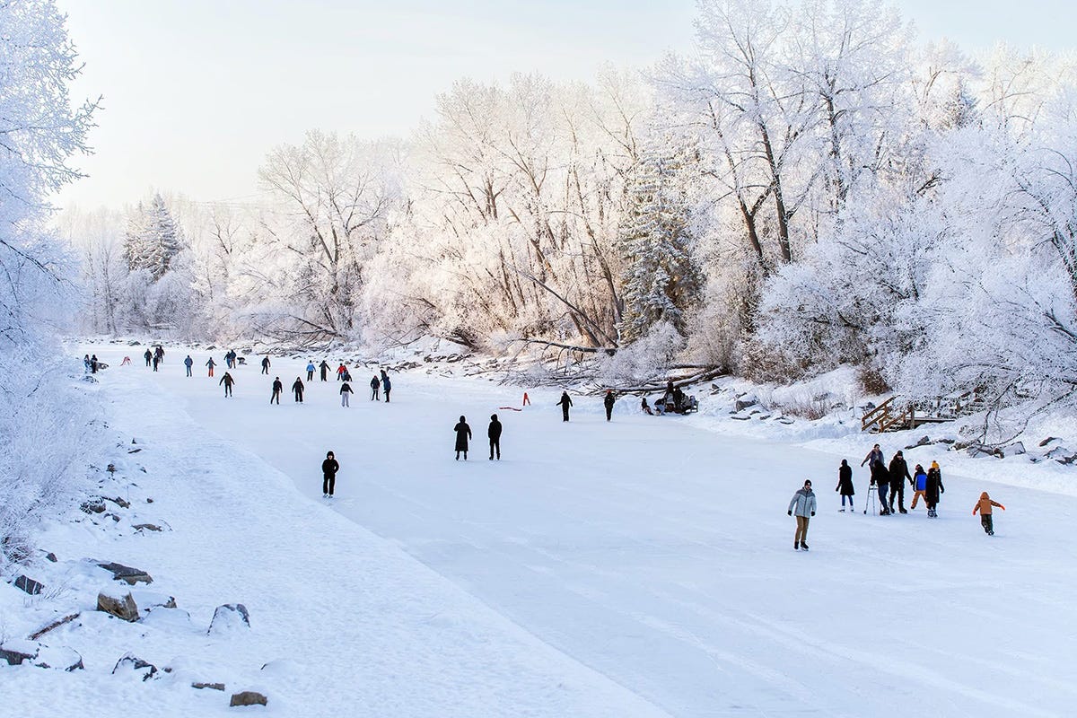Photo of a frozen stretch of water set between heavily frosted trees. Skaters dot the surface as black figures against the frosty white surroundings Photo of a frozen stretch of water set between heavily frosted trees. Skaters dot the surface as black figures against the frosty white surroundings
