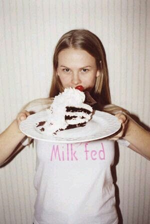 This may contain: a woman holding a plate with a piece of cake on it in front of her face