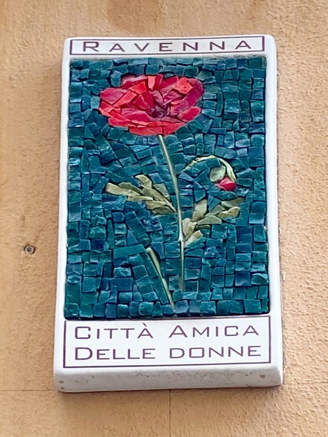 Three mosaic flower wall-plaques depicting a white lily, a white tulip and a poppy, with text declaring Ravenna to be a city friendly to women.